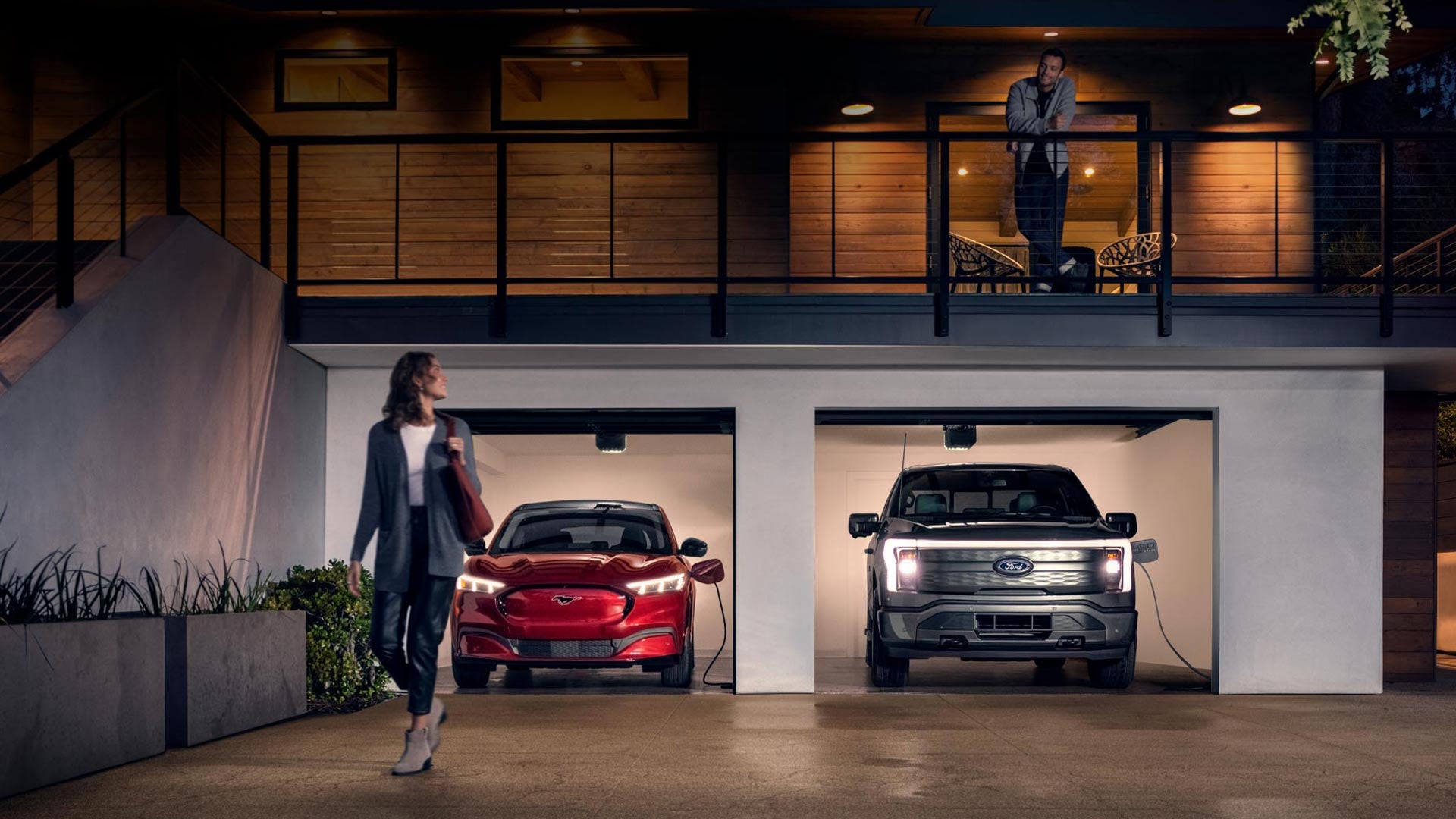 Woman walking out from home garage with a 2024 Mustang® Mach-E and Ford Lightning® truck in plugged-in and charging | Mike Dorian Ford Inc in Clinton Township MI