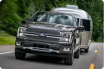 Ford F-150 towing a camper on a tree-lined road
