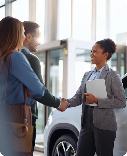 Dealership consultant shaking hands with customers beside a vehicle