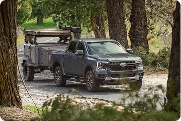 Ford Ranger towing a utility trailer on a wooded road