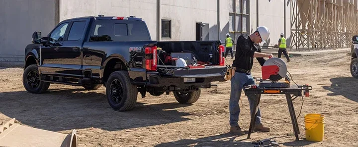 Ford pickup at a construction site with a tradesperson cutting material beside the truck
