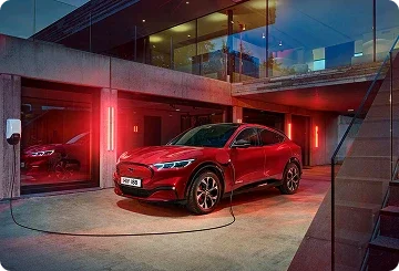 Red Ford Mustang Mach-E plugged in and charging outside a modern home