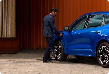 Driver plugging a charging cable into a blue Ford plug-in hybrid SUV