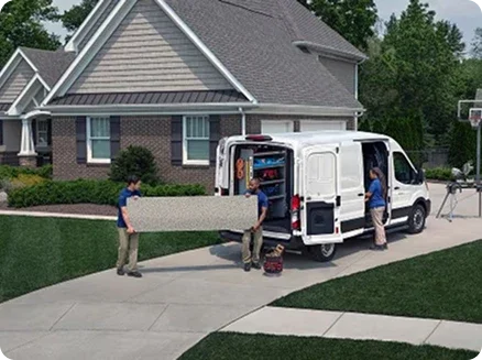 Two workers loading materials into a Ford Transit Cargo Van in a driveway