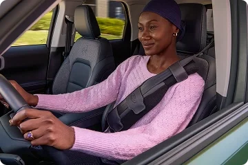 Woman in a pink sweater driving a Ford while wearing the Ford SupportBelt seat-belt accessory
