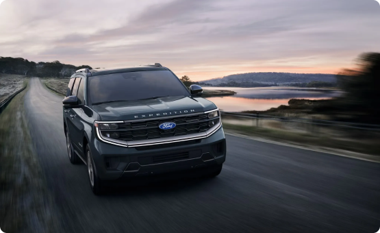 Ford Expedition driving on a lakeside road at dusk